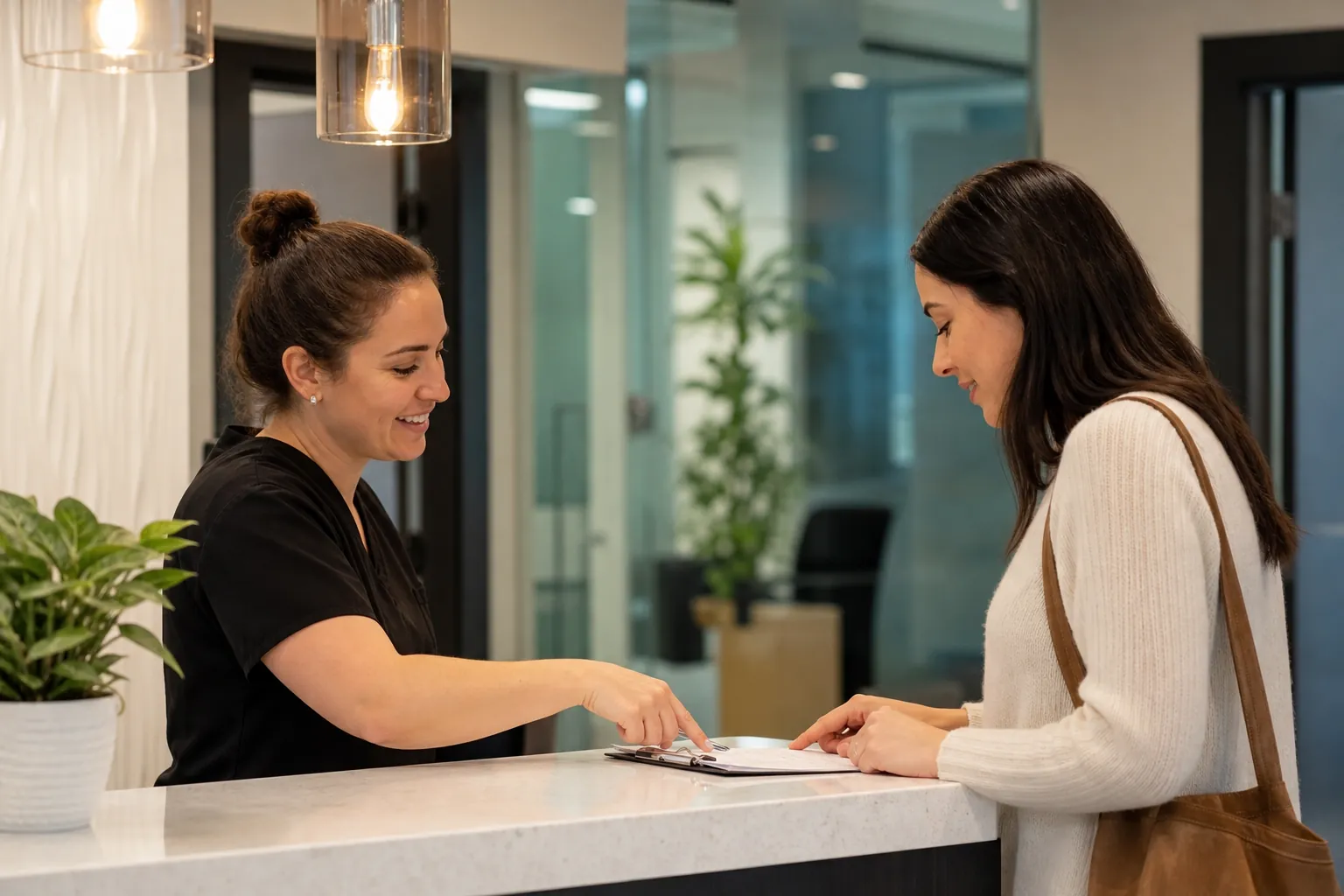 A receptionist in black scrubs points to paperwork on a clipboard as a woman with a brown shoulder bag stands at the counter.